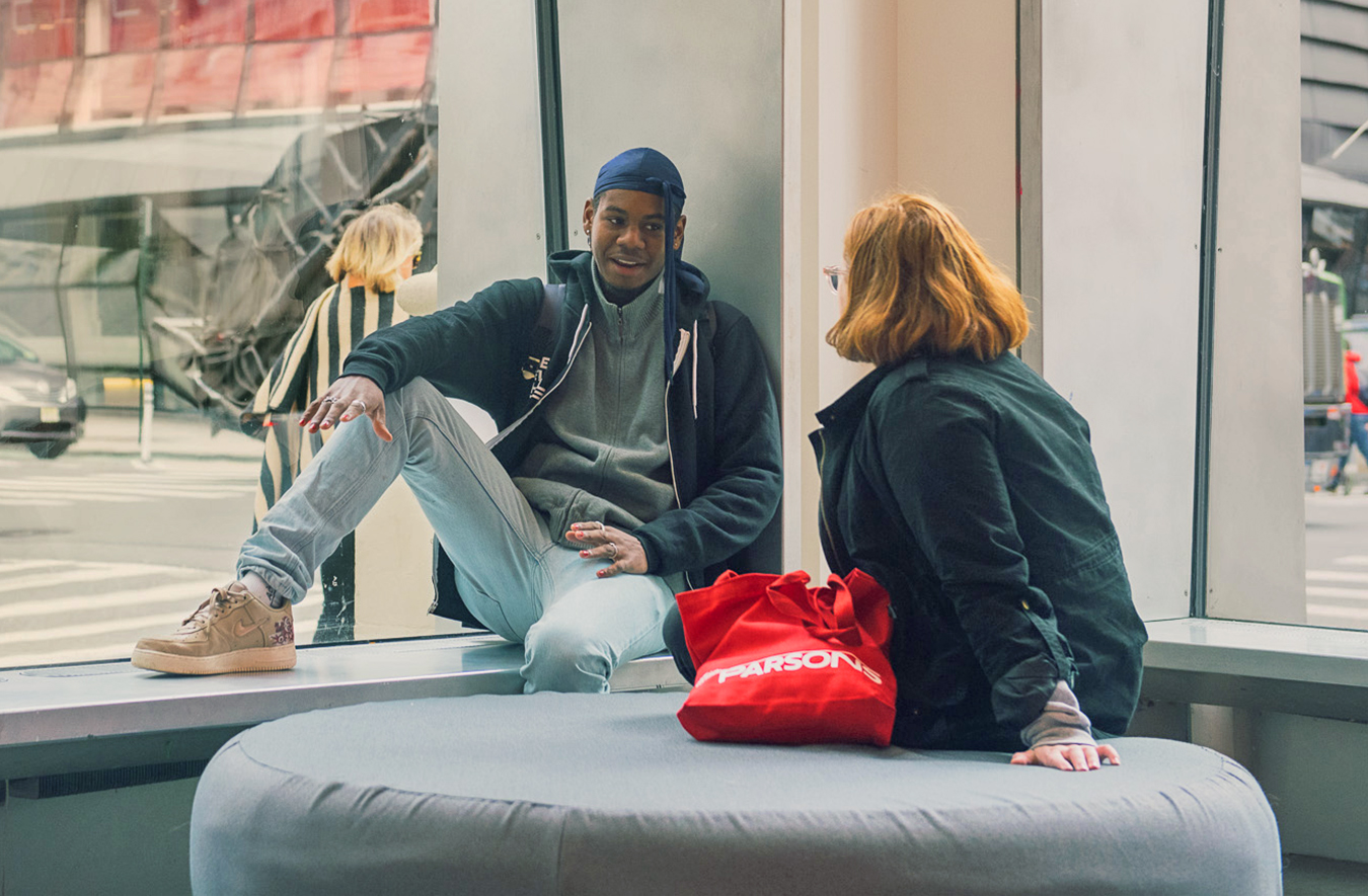 Two students talking sitting in front of a window